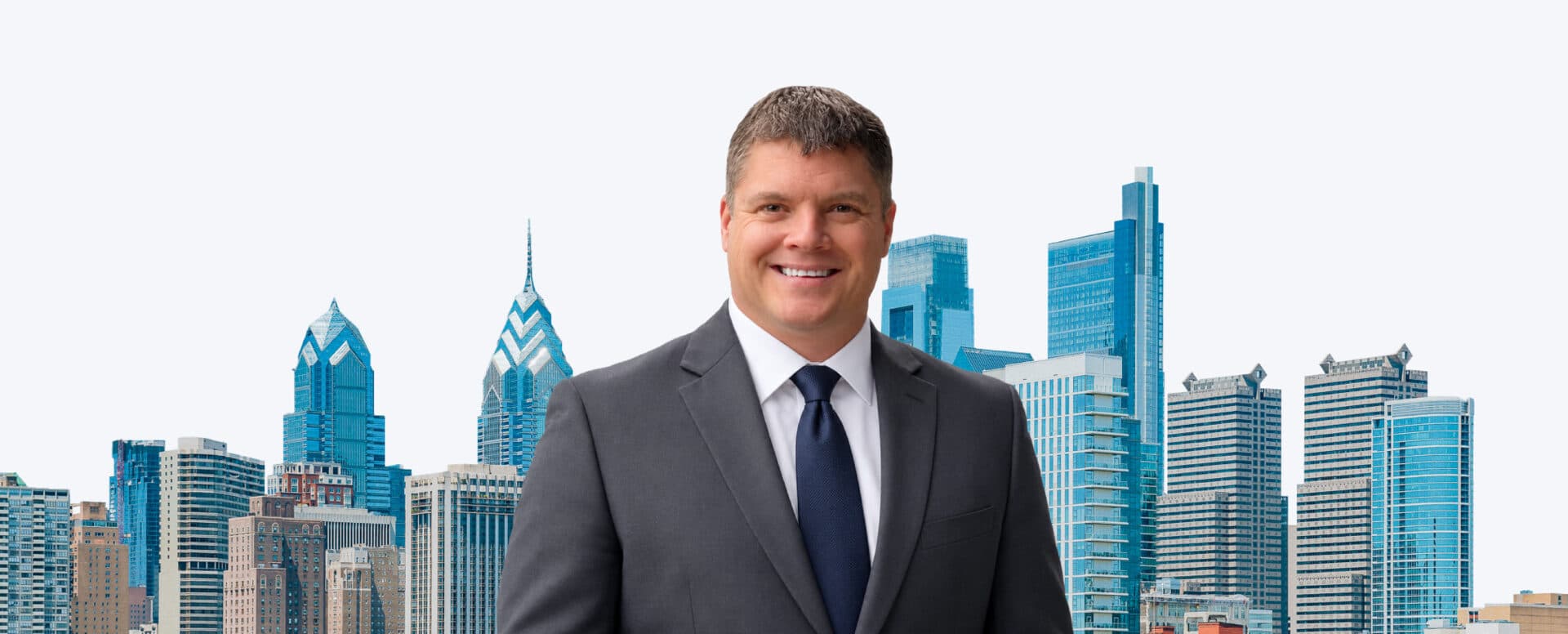 Michael Inforzato in a gray suit and navy tie smiling in front of the Philadelphia skyline, joining the Matthews seniors housing division